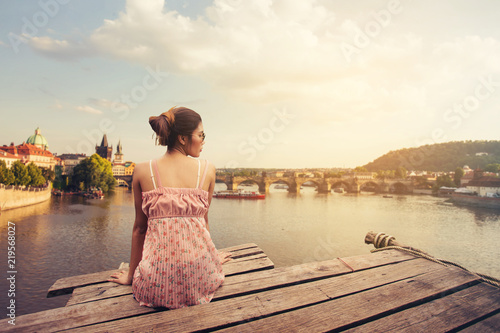 Young woman sitting on wood pier looking Prague Castle, Prague river Vltava and many famous Prague sights and historic architecture, back view. photo