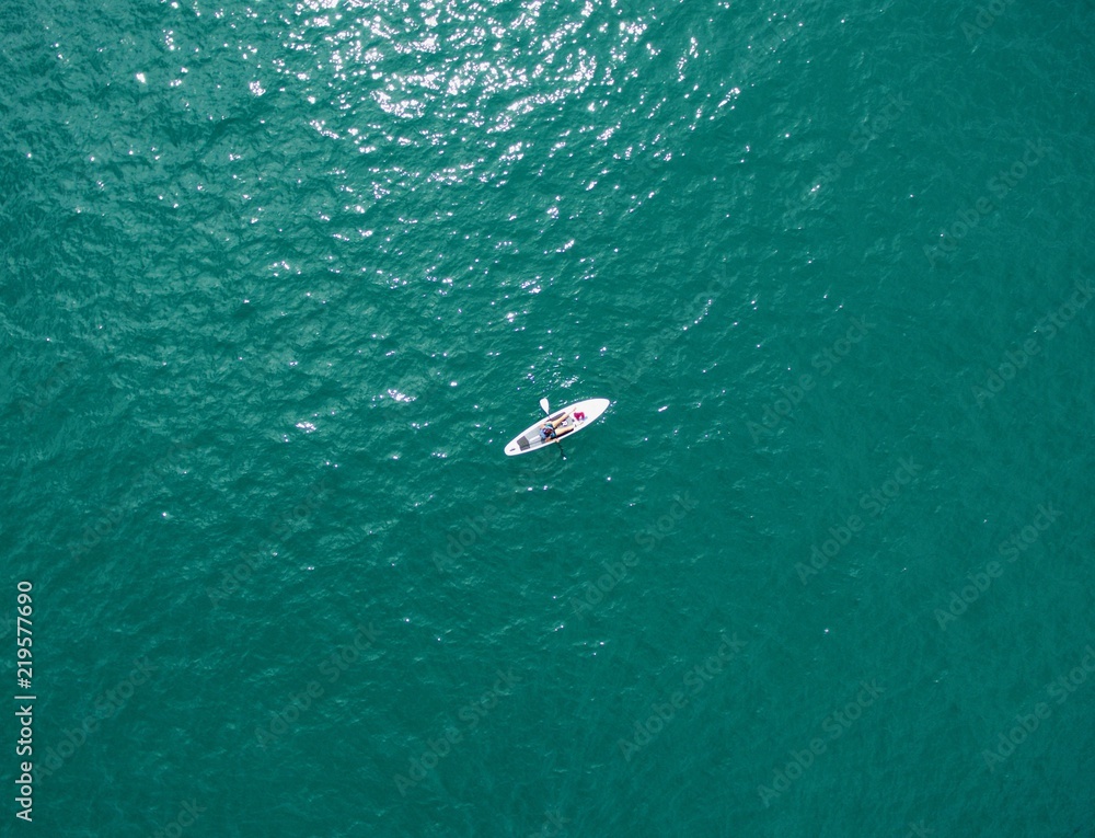 Drone shot, looking directly down on a person on a stand up paddle board in a blue /green ocean