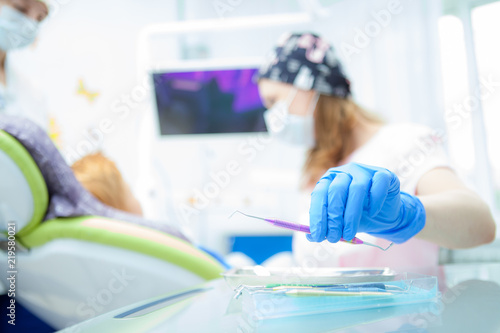 A close-up photo of a dentist s hand taking a sterile instrument from a metal tray. Focus on the doctor s hand