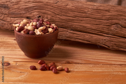Deep fried peanuts in clay bowl over rustic wooden background. Selective focus photo