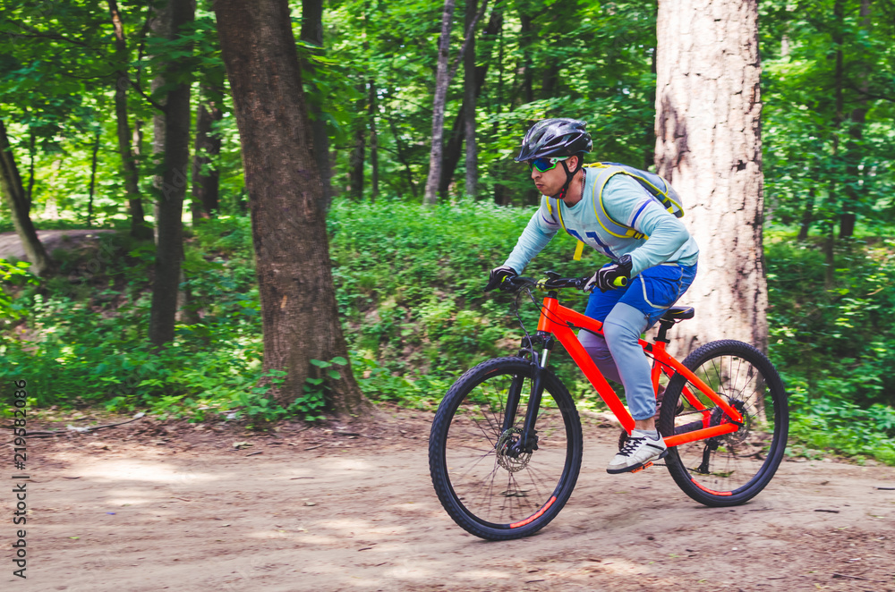 Cyclist in helmet on an orange bike doing a trick in a springboard jump in the forest, motion blur