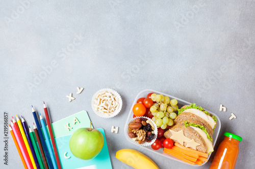 Back to school concept. Healthy lunch box and colorful stationery on gray stone table top view. photo