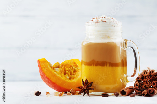 Pumpkin spiced latte or coffee in glass jar on white wooden table. Autumn, fall or winter hot drink.