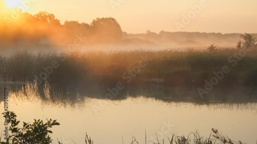 Morning fog on a quiet lake in the rays of the rising sun