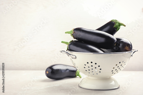 Colander with eggplants on table against light background