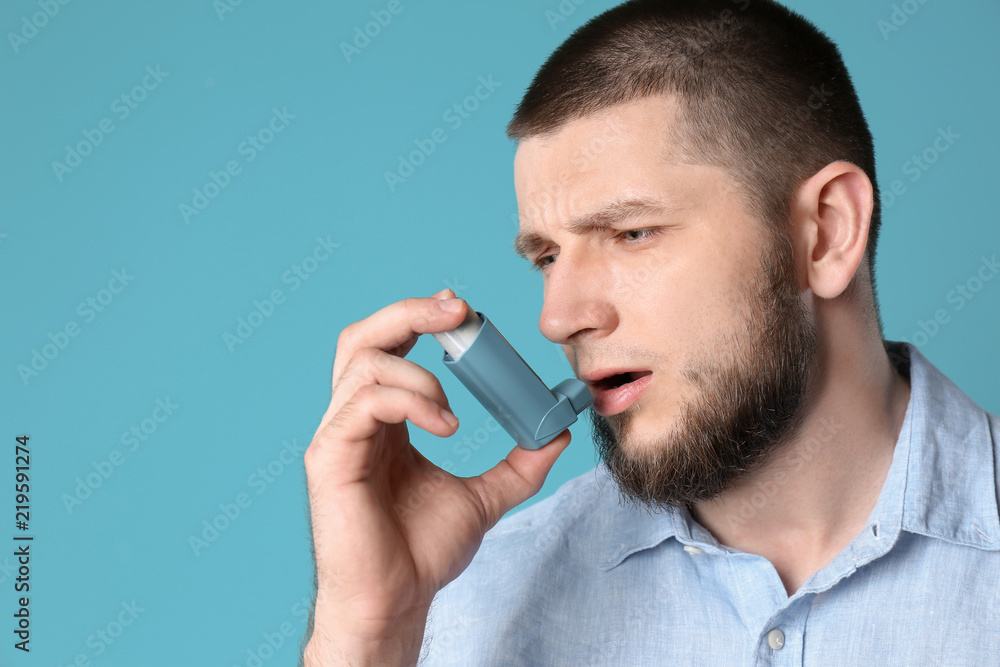 Young man using asthma inhaler on color background Young man using asthma inhaler on color background