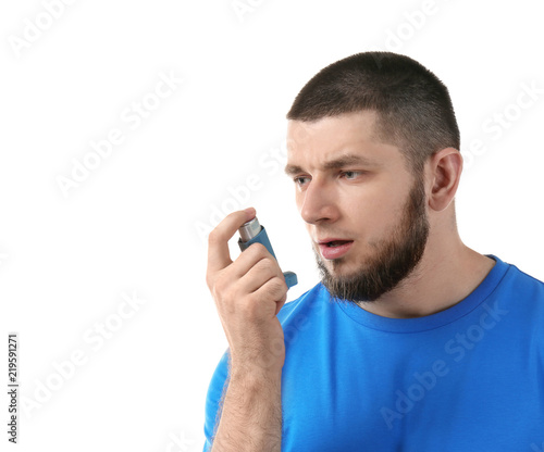 Young man using asthma inhaler on white background