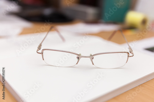 Reading glasses lie on a book on a desk