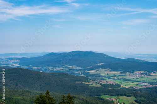 Fototapeta Naklejka Na Ścianę i Meble -  View from top of a mountain in the valley with clouds on the sky and mountains on the background and stones and trees in front of in the bavarian forest