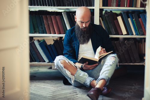 Handsome bearded man sitting on floor, reading book and relaxing