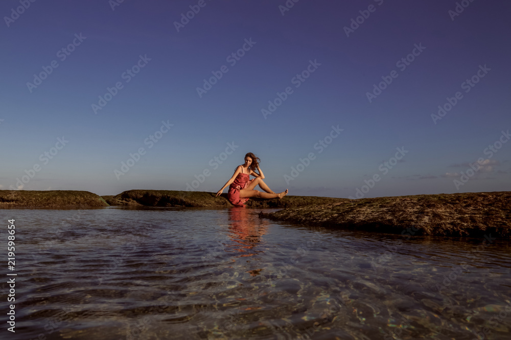 Young woman in the red dress enjoying her vacation time on the empty remote beach