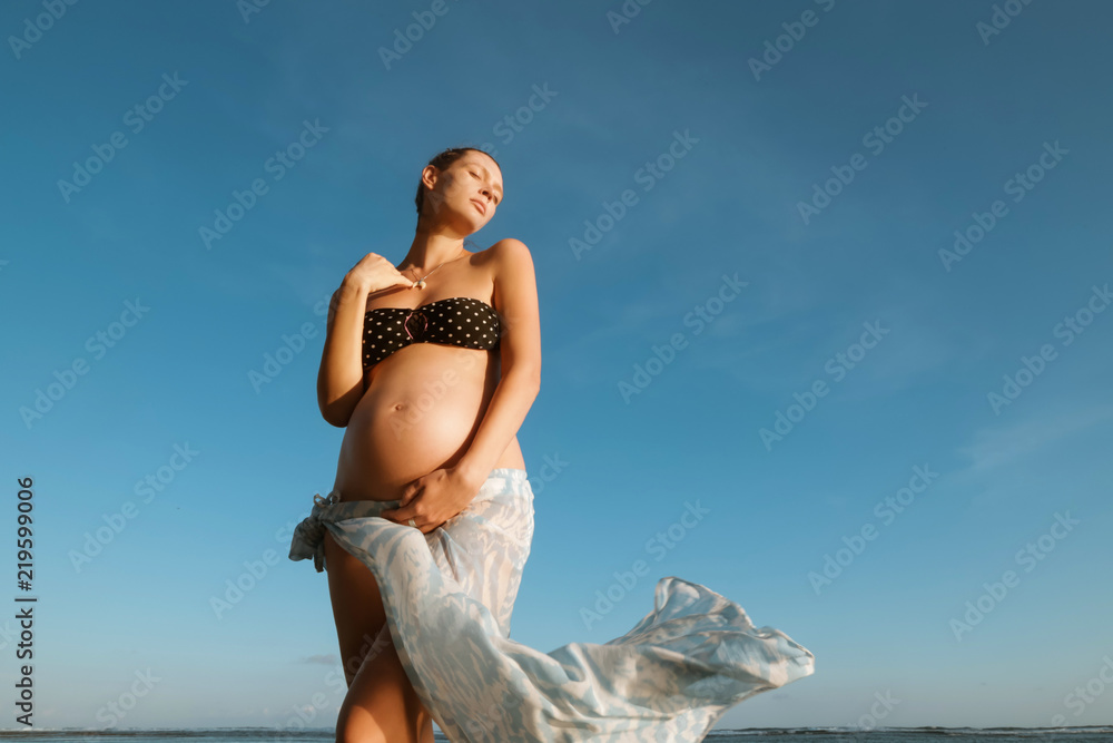 Portrait of young pregnant woman against the clear blue sky, vacation during pregnancy time concept