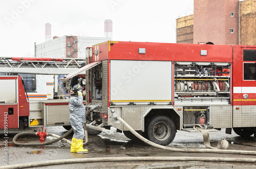 The employee of service of rescue about the fire truck the rescuer is on duty at special equipment for ensuring fire safety. Rescuers in capsule suits put a water obstacle on the way of a cloud of tox