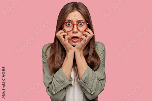 Billede på lærred Horizontal shot of fearful young female looks with alarmed nervous expression, recieves tragic news