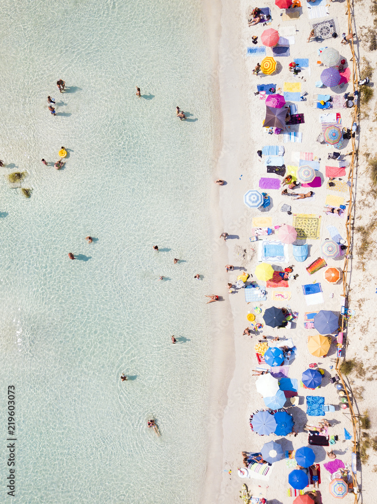 Aerial view of a white beach full of colored beach umbrellas and relaxed people swimming on a clear sea. Cala Brandinchi, Sardinia, Italy.