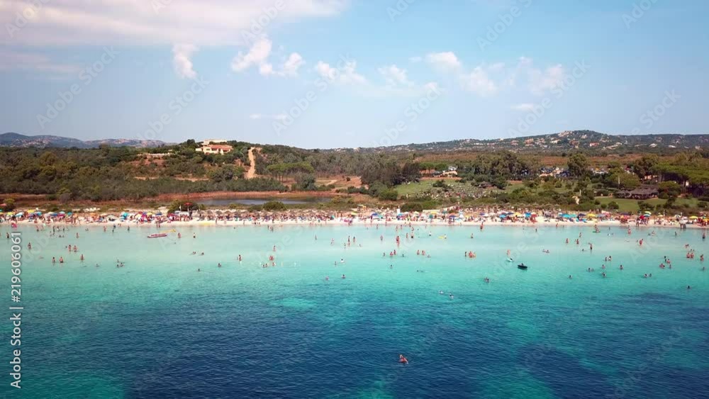 Aerial view of a white beach full of colored beach umbrellas and relaxed people swimming on a clear sea. Aerial view of a white beach full of colored beach umbrellas and relaxed people swimming on a clear sea.