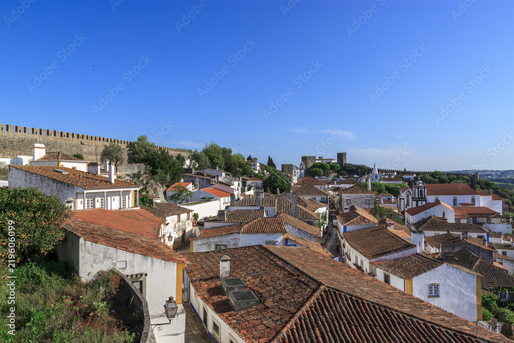 Scenic view of white houses red tiled roofs, and castle from wall of fortress. Beautiful old town with medieval. Obidos village, Portugal. Summer sunny day.
