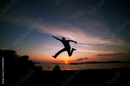 Asian man traveler is jumping on top of a rainforest mountain in scenery sunrise or sunset time background.