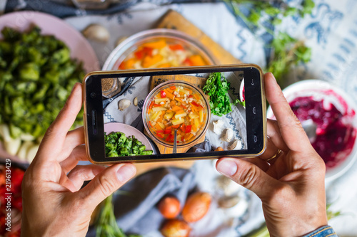 Woman hands make smartphone food photography of corn, potato, pepper vegetables hot soup. Trendy phone food photo for social media or blogging. Vegan lunch, vegetarian dinner, healthy diet. Top view