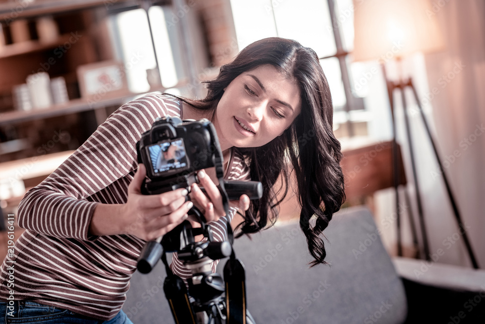 Great gadget. Smiling dark-haired woman fixing her camera while making a video for her blog Great gadget. Smiling dark-haired woman fixing her camera while making a video for her blog