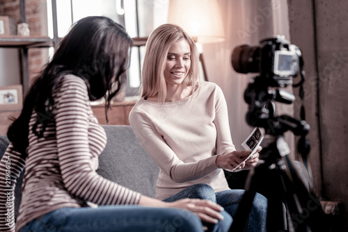 Check this out. Content blond woman smiling while showing photos to her friend