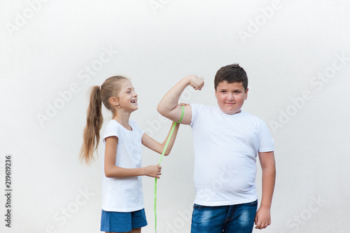 Obraz na płótnie pretty laughing thin little girl measuring cute fat boy biceps muscle with tape