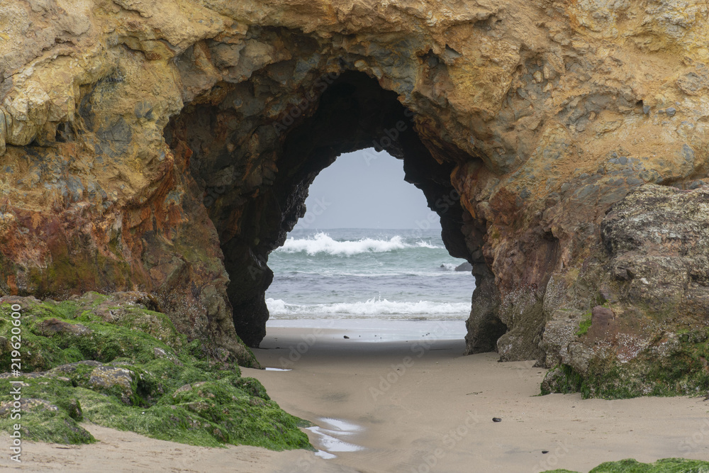 The natural arch at Pescadero State Beach in California during low tide with ocean waves in the background. 