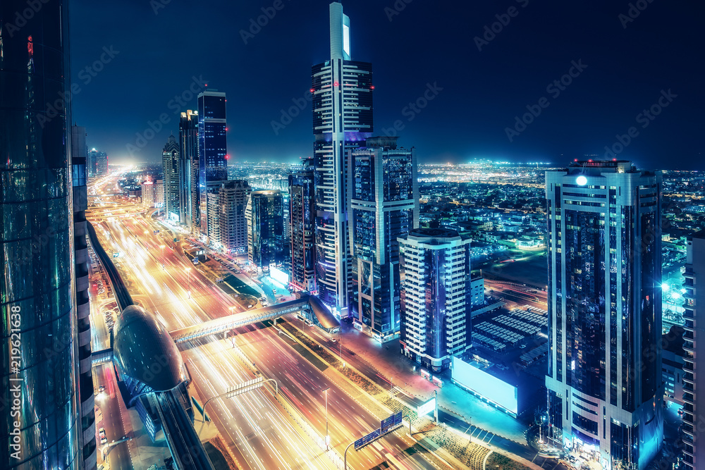 Fototapeta premium Colorful skyline of a big modern city with illuminated skyscrapers and highways. Aerial view over downtown Dubai, UAE. Travel and architectural background.