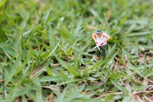 Close up of Miniature figure Senior gardener in garden cutting grass with scissors.