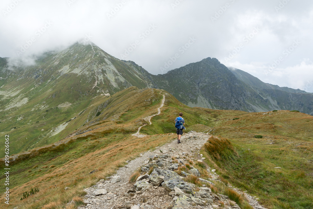 young tourist with a wooden stick walking on a mountain trail