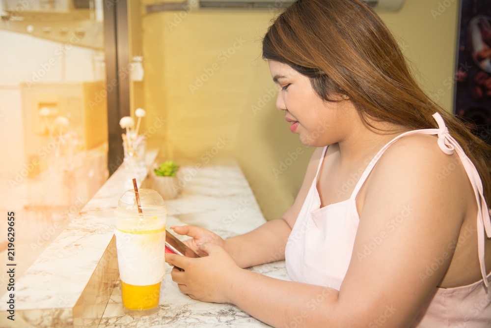 Portrait of Pretty Asian fat woman drinking orange juice and used mobile in a coffee shop. Portrait of Pretty Asian fat woman drinking orange juice and used mobile in a coffee shop.
