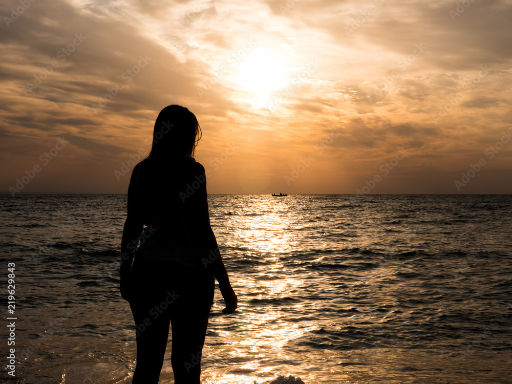 Woman silhouette watching sun on the beach at sunset.. Tourist girl on beach holiday