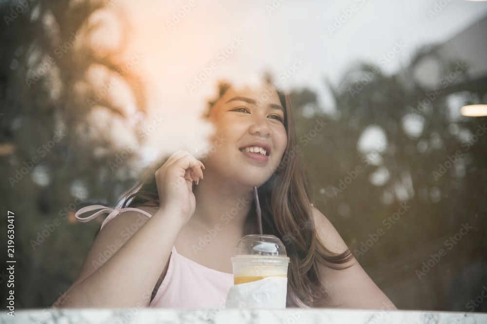 Portrait of Pretty Asian fat woman drinking orange juice and used mobile in a coffee shop. Portrait of Pretty Asian fat woman drinking orange juice and used mobile in a coffee shop.
