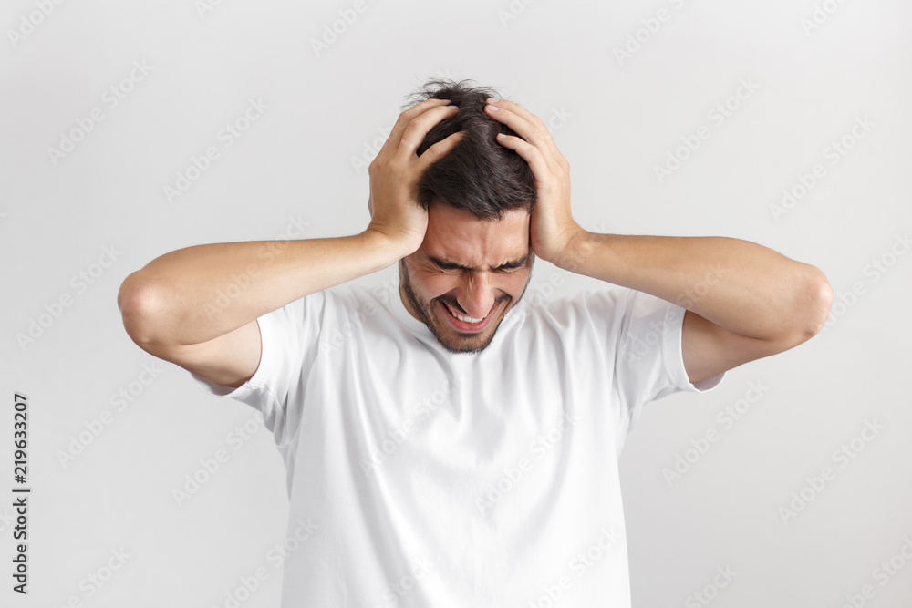 Upset unhappy young man squeezing head with hands, suffering from headache. People, stress, tension and migraine concept. Upset unhappy young man squeezing head with hands, suffering from headache. People, stress, tension and migraine concept.