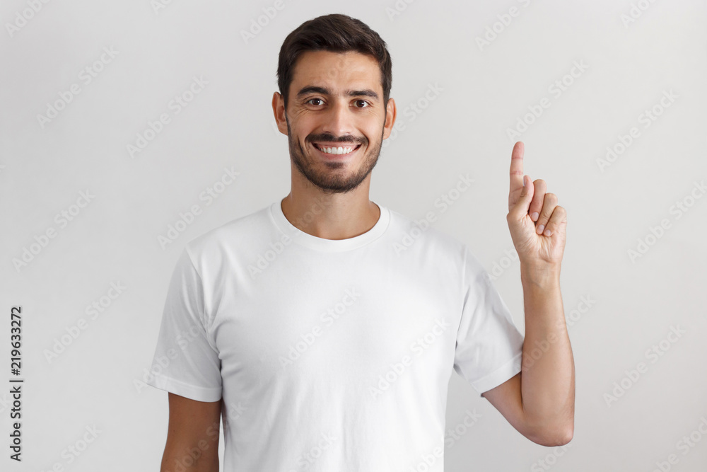 Handsome young man in white t-shirt pointing up with his finger isolated on gray background Handsome young man in white t-shirt pointing up with his finger isolated on gray background