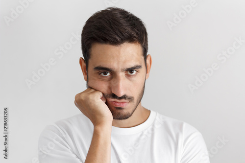 Close up portrait of bored young man in white tshirt with head on chin isolated on gray background