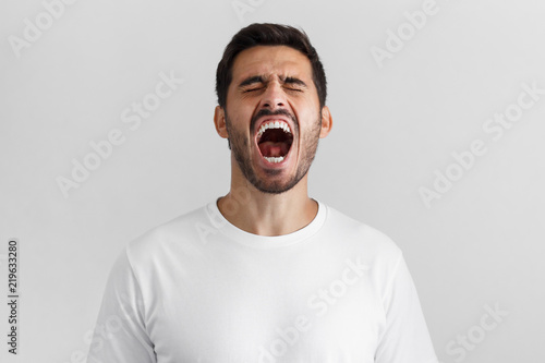 Konstfotografi Screaming with closed eyes crazy young man in blank white t-shirt isolated on gr