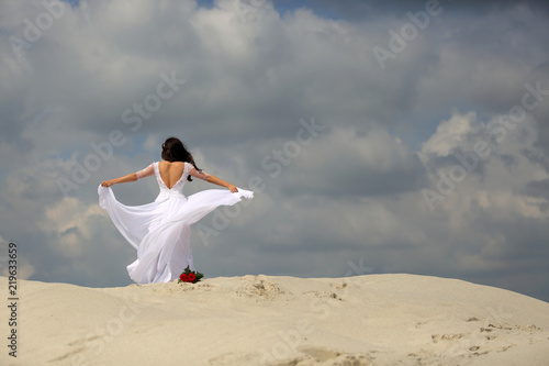Piękna dziewczyna w białej sukni tańczy na szczycie piaszczystej wydmy, pustynia.