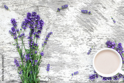 Fototapeta Naklejka Na Ścianę i Meble -  Lavender flowers bouquet with cup of cappuccino and frame made of flowers on rustic wooden background. top view