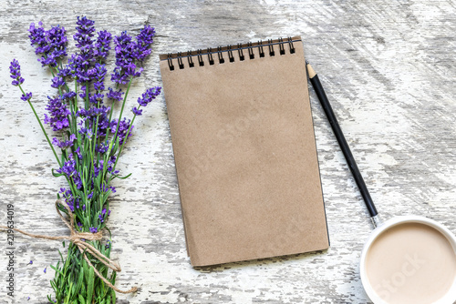 Fototapeta Naklejka Na Ścianę i Meble -  lavender flowers bouquet, blank vintage notebook with pencil and cup of cuppuccino over white wooden table. top view