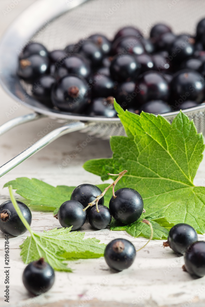 Berries of black currant in colander close-up. Black currant close-up on table. Background of black currant berries. Berries of black currant in colander close-up. Black currant close-up on table. Background of black currant berries.