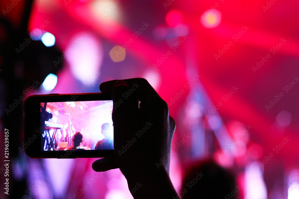 Smartphone shooting festival concert. Blurred music stage bokeh background for design. Fans takes picture of scene on phone