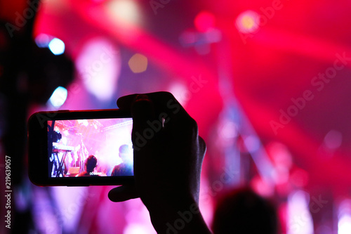 Smartphone shooting festival concert. Blurred music stage bokeh background for design. Fans takes picture of scene on phone