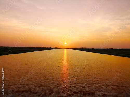 The travelling and life concept. The sun is falling in the dusk. The golden light of the sun reflects on the water surface with many small wave of the river. Selective focus and copy space.