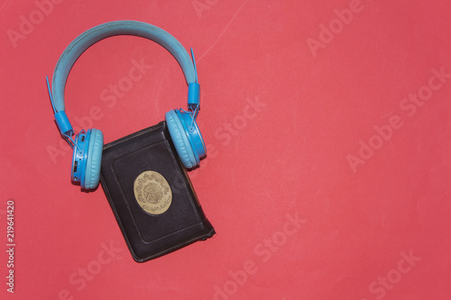 listen to quran concept, holy muslim book and bluetooth headphone isolated on red background