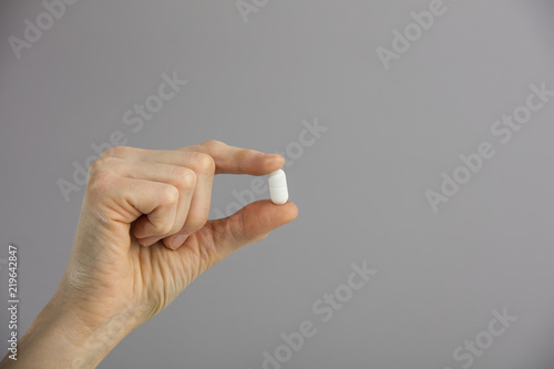 A woman holds a white medicine between her fingers.