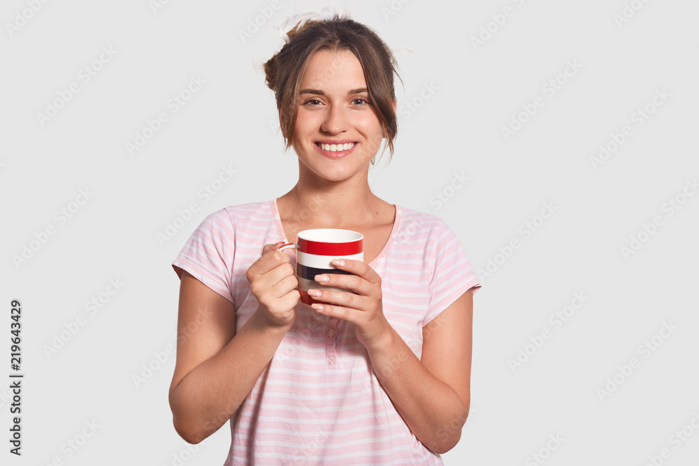 Happy brunette young woman has good mood in morning, drinks hot coffee, talks with husband, discuss plans on day, dressed in pyjamas, isolated over white background. People, morning time concept Happy brunette young woman has good mood in morning, drinks hot coffee, talks with husband, discuss plans on day, dressed in pyjamas, isolated over white background. People, morning time concept