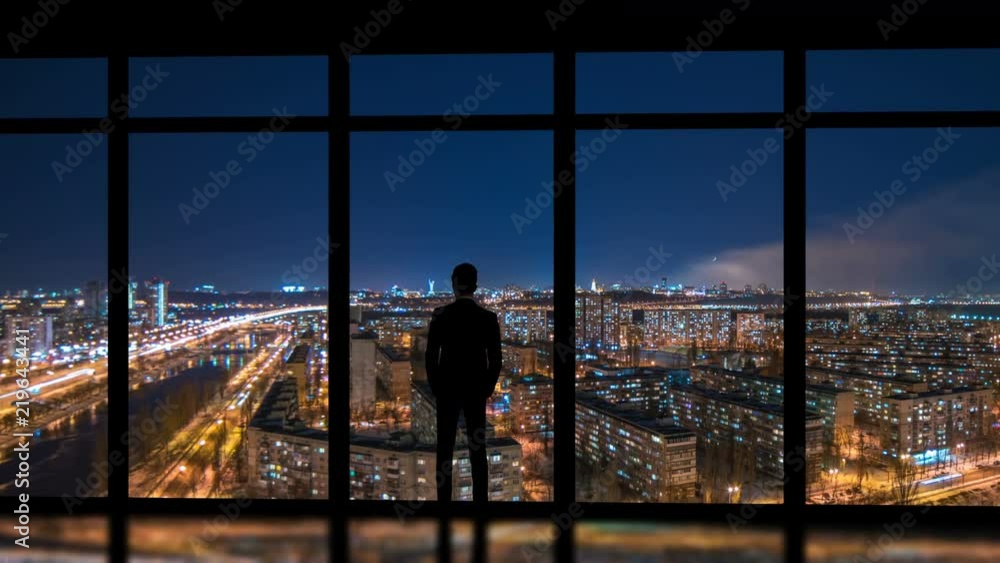 The man standing near windows on a night metropolis background. time lapse