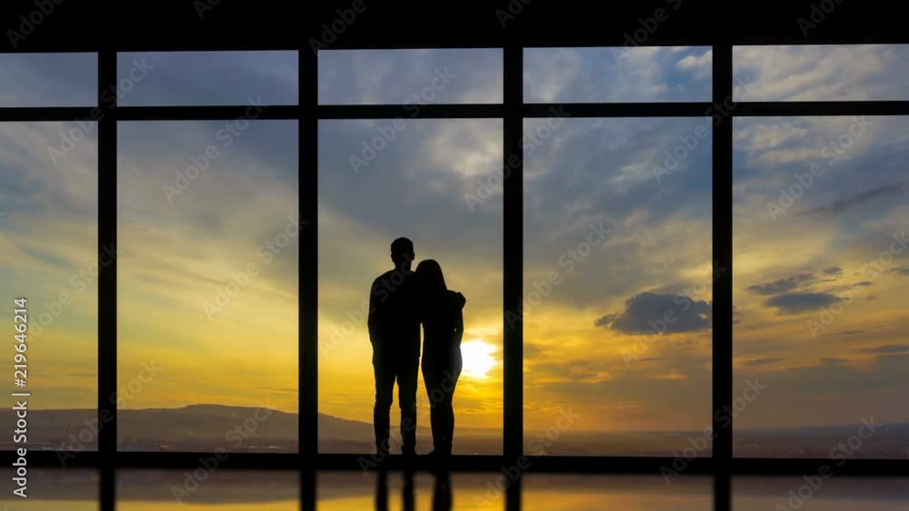 The man and woman standing near windows on a sunset background. time lapse The man and woman standing near windows on a sunset background. time lapse