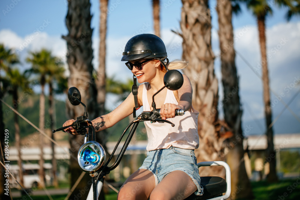 E Bike Rider girl riding on bike trail on Sunday morning. Pretty joyful woman riding electric bicycles wearing summer clothing protective helmets and sunglasses enjoying ride. Stock Foto Adobe Stock